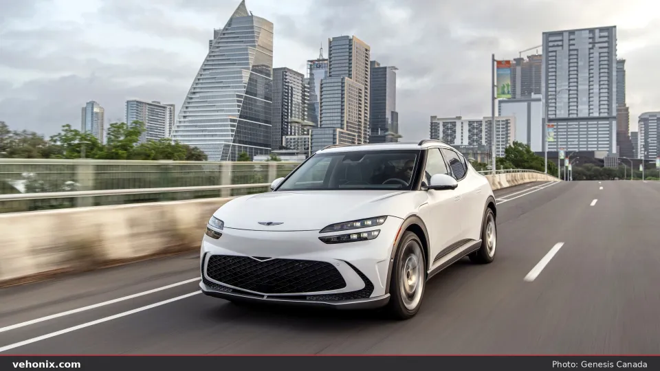 2026 Genesis GV60 Advanced in white, front three-quarter driving on a city bridge