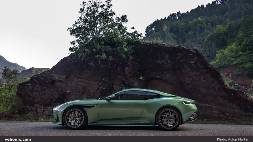 2026 Aston Martin DB12 in Iridescent Emerald, side profile on a mountain road by a rock face