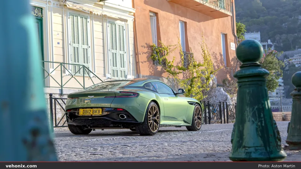 2026 Aston Martin DB12 in Iridescent Emerald, rear three-quarter on a cobblestone street