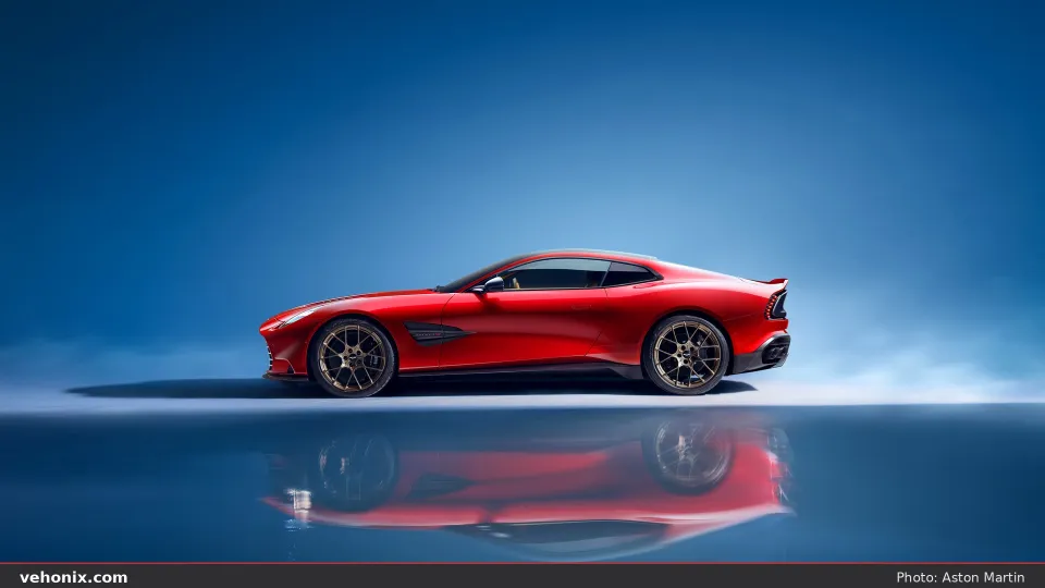 2026 Aston Martin Vanquish in red, side profile on a reflective blue studio floor