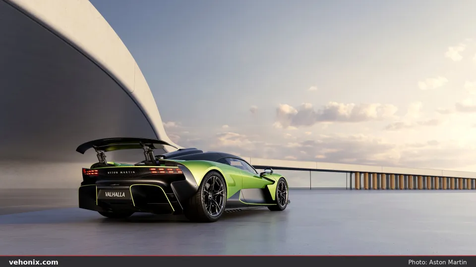 2026 Aston Martin Valhalla in lime green, low rear view with raised wing beside modern architecture