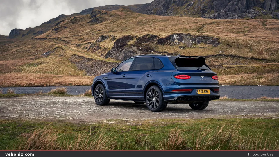 2026 Bentley Bentayga EWB in blue, rear three-quarter view by a highland lake