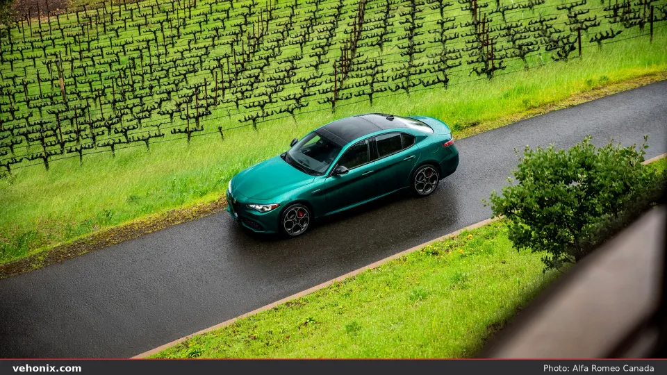 2026 Alfa Romeo Giulia Veloce in metallic green, high-angle view on a wet road by a vineyard