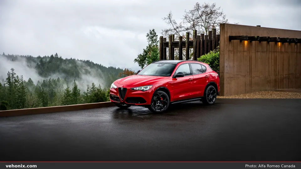 2026 Alfa Romeo Stelvio Veloce in red, front three-quarter view with misty forest backdrop