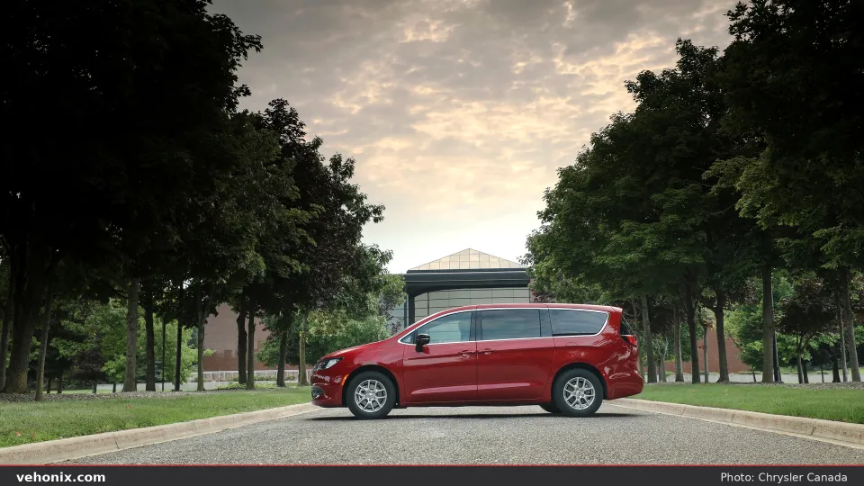 2026 Chrysler Grand Caravan in red, full side profile on a tree-lined road at dusk