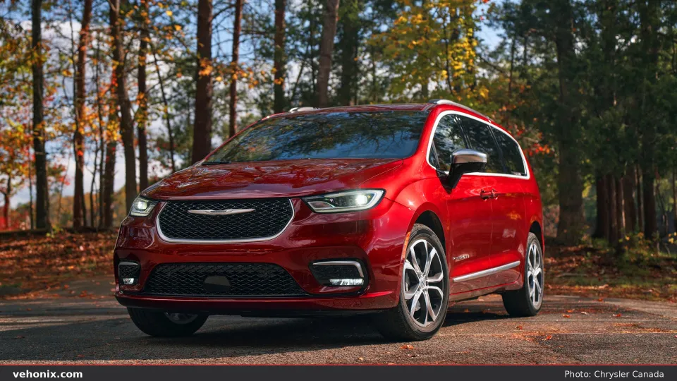 2026 Chrysler Pacifica in red, front three-quarter on a leaf-strewn road in a forest