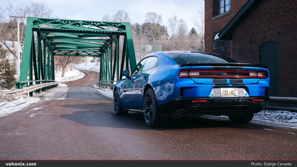2026 Dodge Charger Scat Pack in blue with black stripes, rear three-quarter by a bridge
