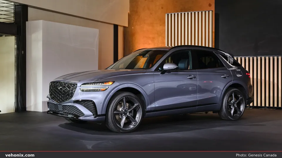 2026 Genesis GV70 in dark grey, front three-quarter in a warm wood-paneled studio