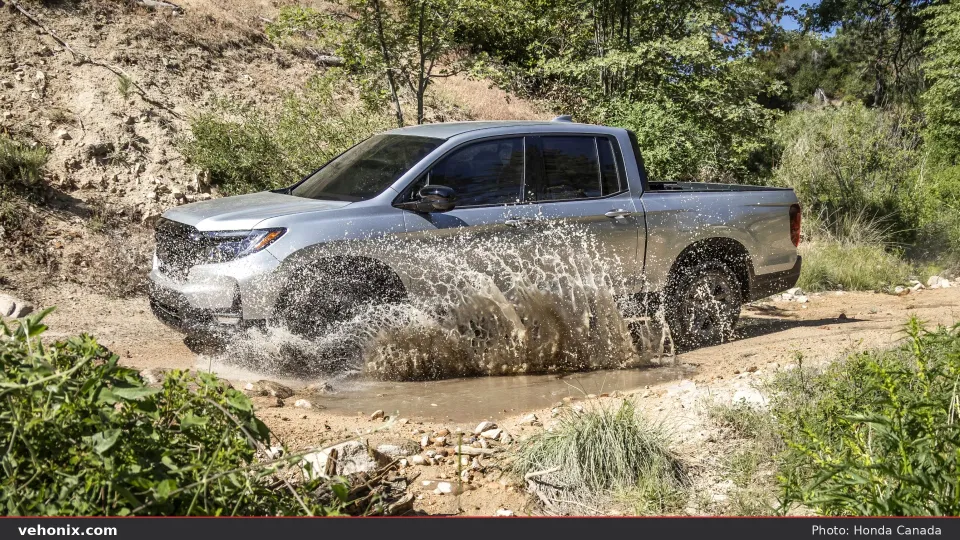 2026 Honda Ridgeline in silver, front three-quarter splashing through a muddy trail