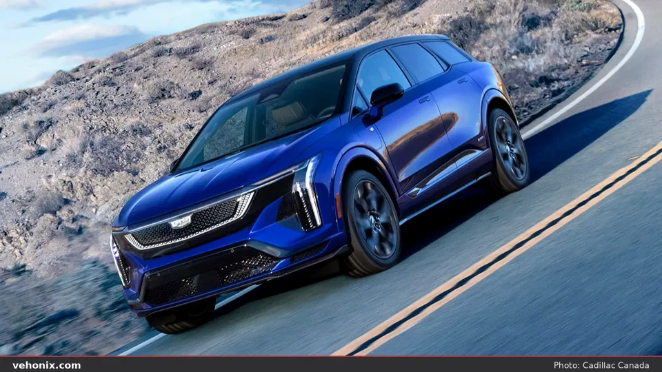 2026 Cadillac OPTIQ-V in blue with black roof, front three-quarter on a mountain road