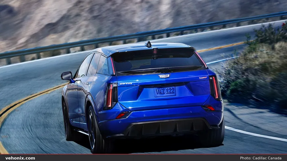 2026 Cadillac OPTIQ-V in blue, rear three-quarter driving on a winding mountain road
