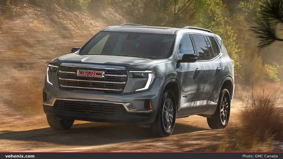 2026 GMC Acadia in silver, front three-quarter driving on a sunlit dirt trail