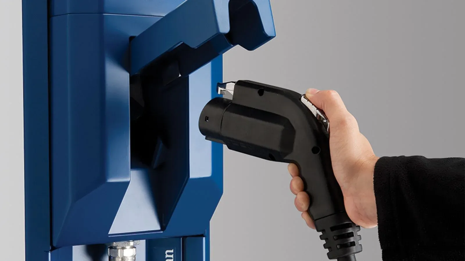 A hand plugging a J1772 charging connector into its holder on a blue Circuit électrique Level 2 station