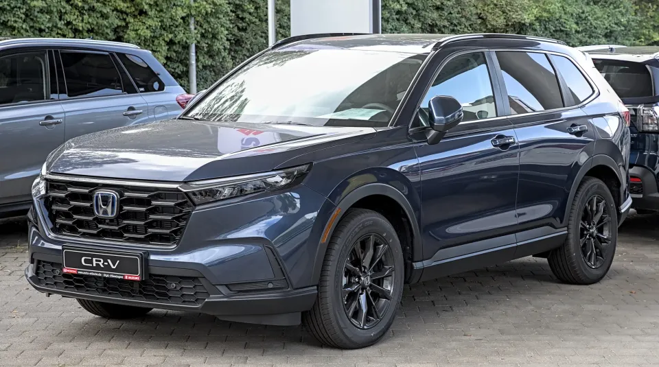 Un Honda CR-V hybride bleu foncé aux roues noires garé sur des pavés, vu de l'avant gauche