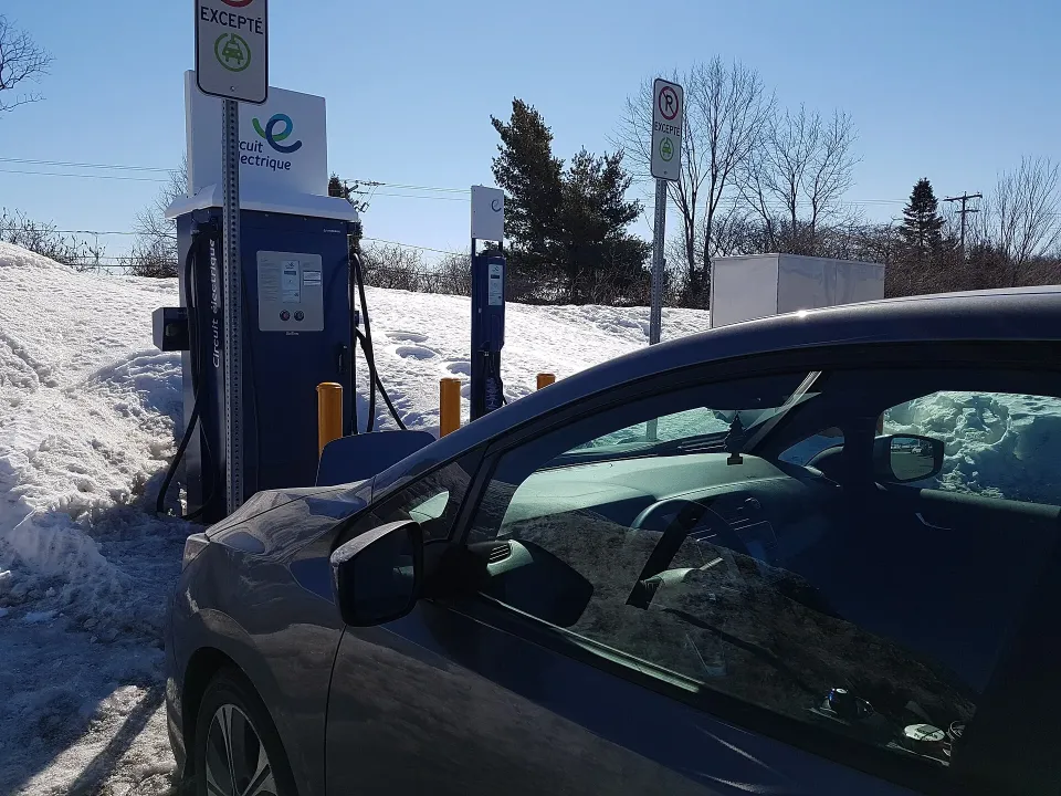 A Circuit électrique fast charger beside snowbanks in Quebec, with an EV parked in front