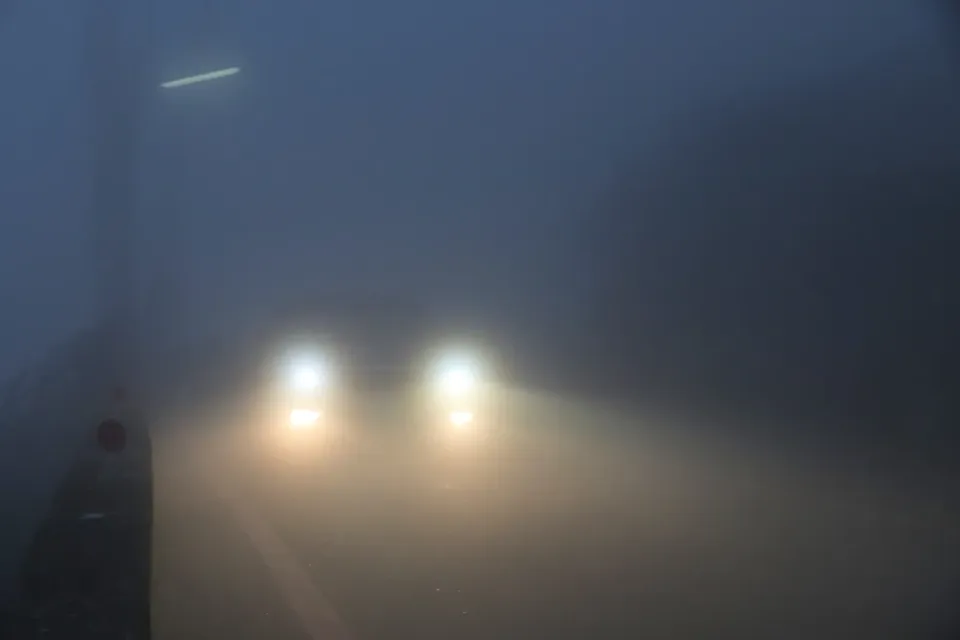 Des phares d'auto allumés dans un épais brouillard sur une route sombre
