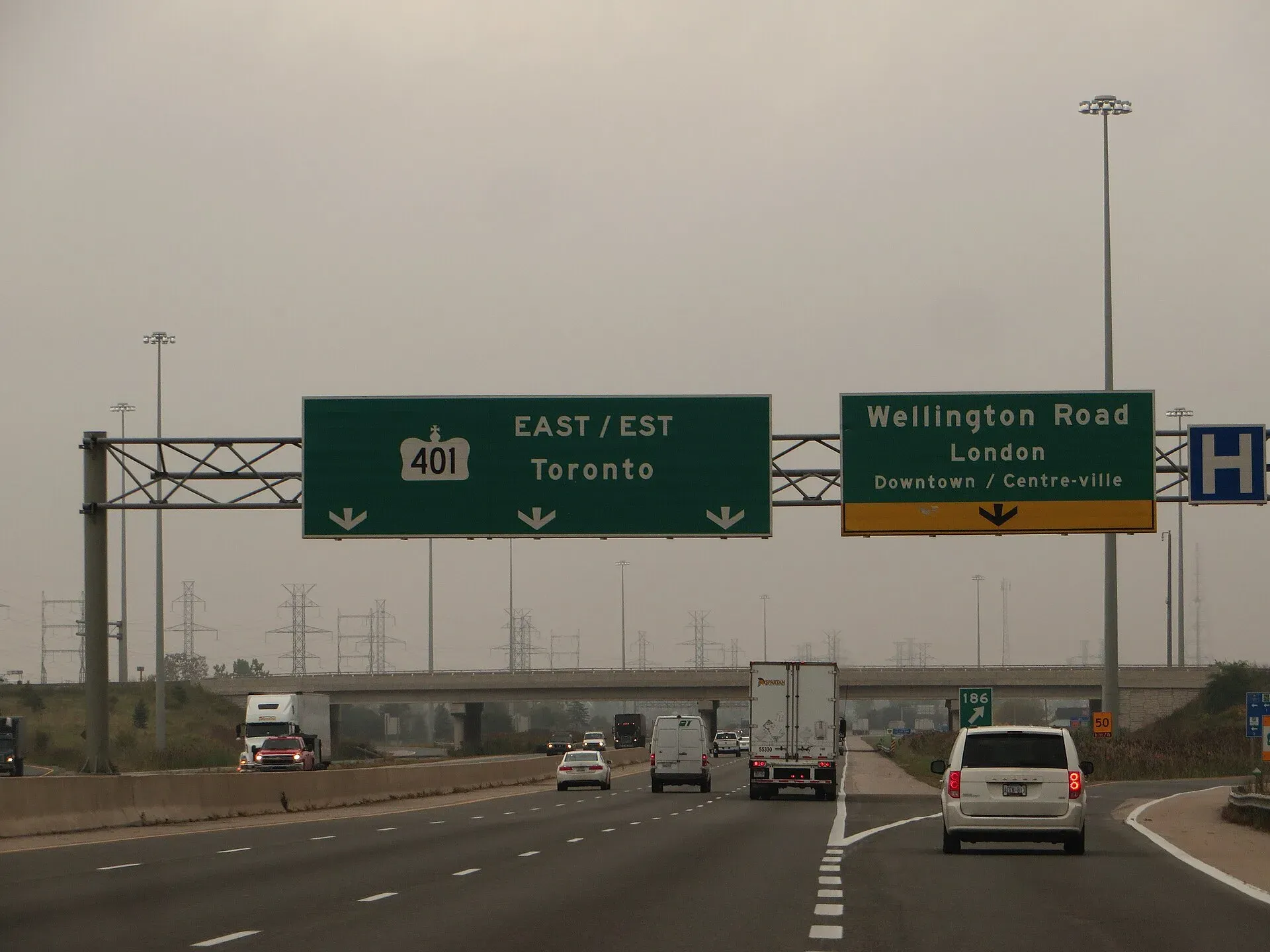 Highway 401 in London, Ontario, with cars, a van and a transport truck under green exit signs for Toronto and Wellington Road