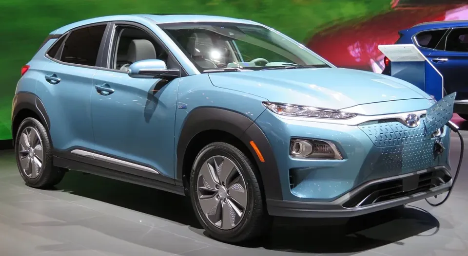 A light blue Hyundai Kona Electric plugged in at a charger