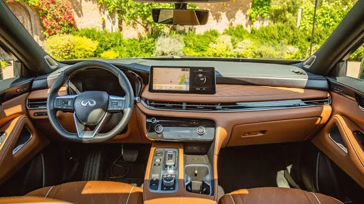 Infiniti QX60 interior seen from the rear seat, showing the dashboard and tan leather seats