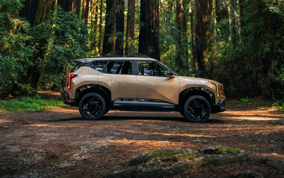 Tan 2027 Kia Seltos parked in a forest clearing, side view