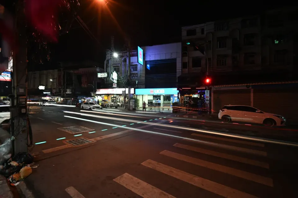 A city crossing at night with car light trails and a striped crosswalk in the front