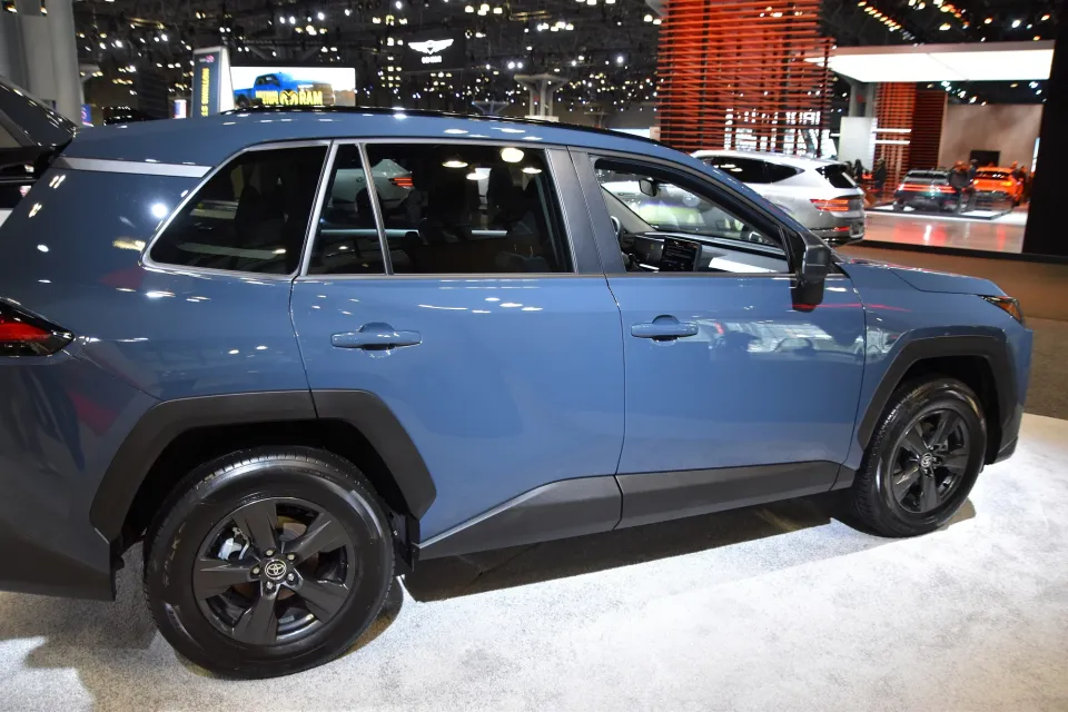 Un Toyota RAV4 LE hybride AWD 2026 bleu aux roues noires, vu de côté dans un salon de l'auto intérieur