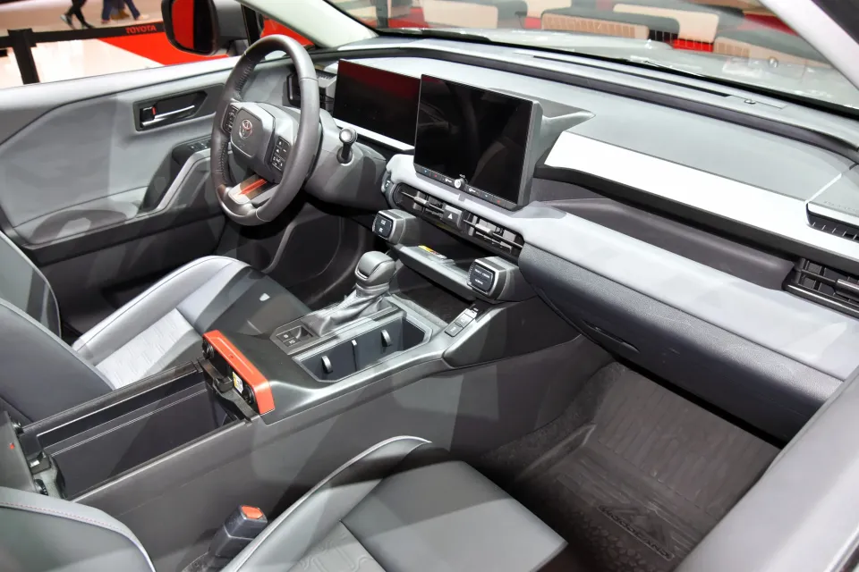 Sièges avant et tableau de bord d'un Toyota RAV4 Woodland hybride 2026 avec deux écrans et des touches orange