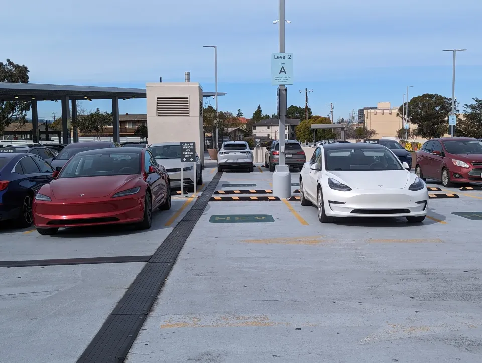 Red Tesla Model 3 with updated styling parked beside a white earlier-generation Model 3 in a parking garage