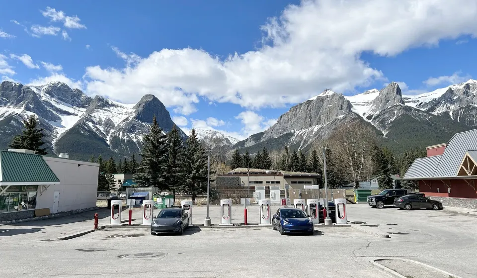 A row of Tesla Supercharger stalls in a parking lot with snowy mountains behind