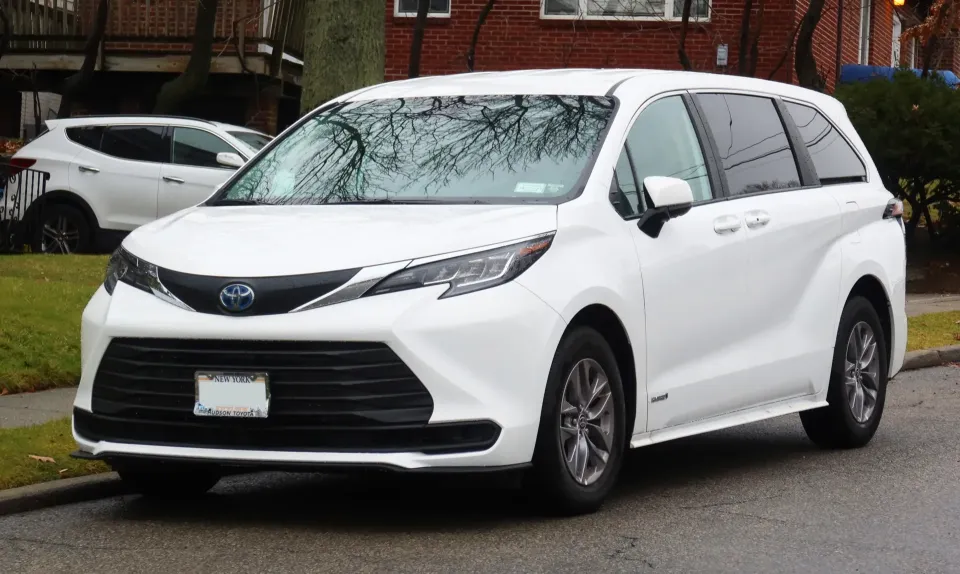 A white 2021 Toyota Sienna Hybrid LE minivan parked on a street, seen from the front left