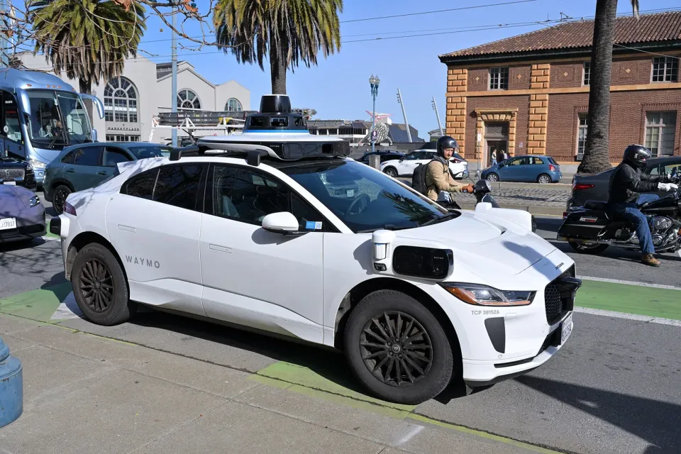 A white Waymo Jaguar I-PACE robotaxi with roof sensors parked on a city street