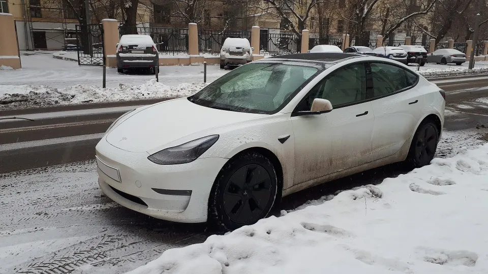 A white Tesla electric sedan parked on a snowy street