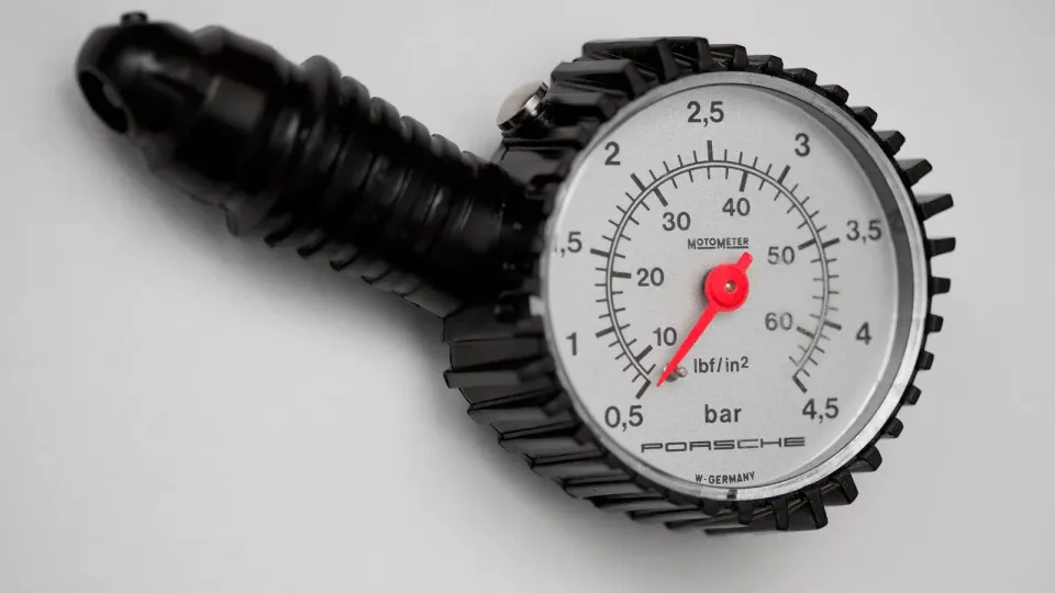 A round tire pressure gauge with a red needle and both psi and bar scales