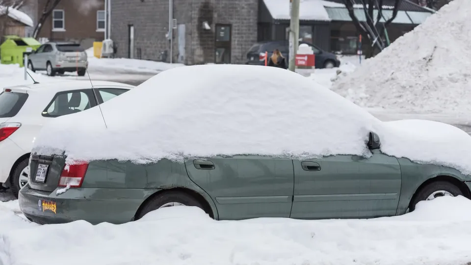 A green sedan buried in snow on a Quebec City street, with other parked cars and snowbanks behind it
